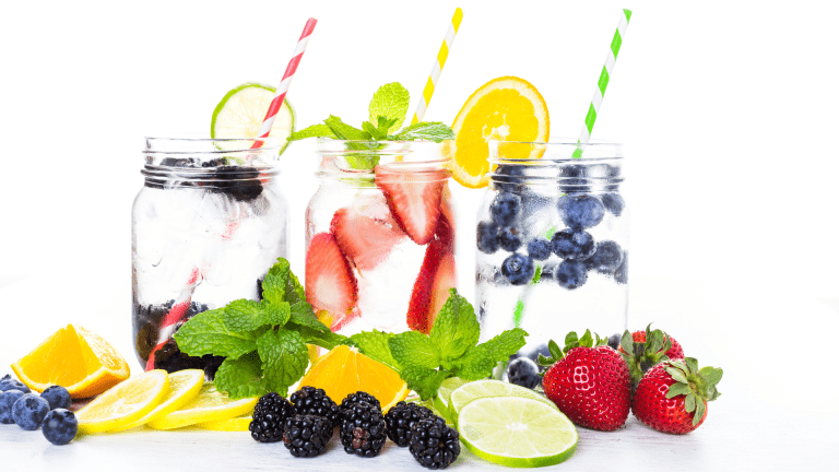 Three jars of fruit-infused water with strawberries, blueberries, lemon, lime, and fresh mint on a white background.